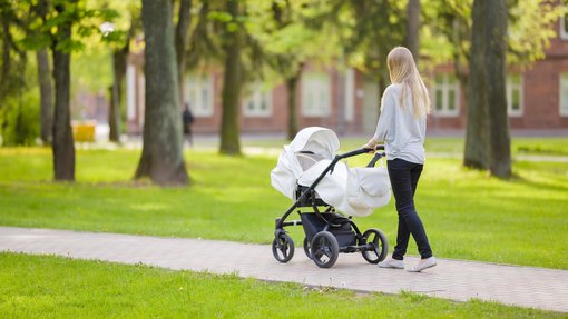 Frau schiebt Kinderwagen im Garten