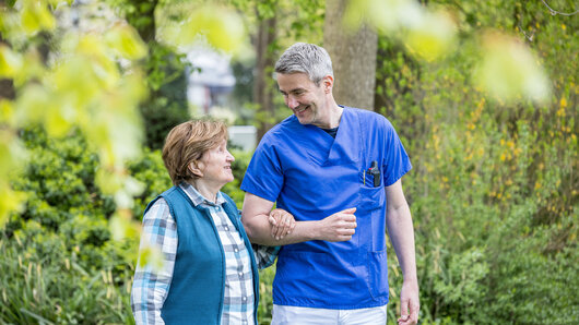 Ein Klinikmitarbeiter geht mit einer Patientin im Garten spazieren